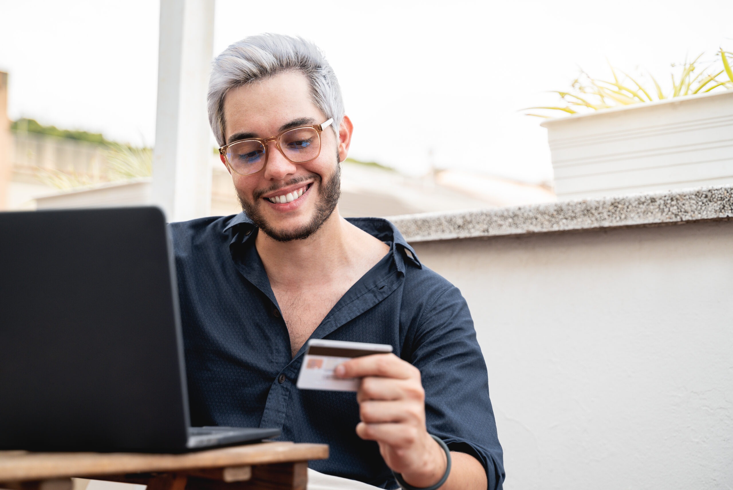 Young hipster man holding credit cart using computer laptop for online payment - E-commerce, internet bank -Focus on face